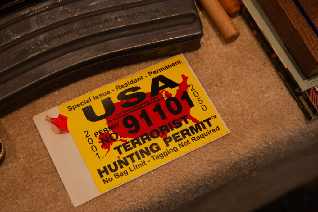 A sticker that reads "USA Terrorist Hunting Permit" on a display table. The sticker is bright yellow with black text and a geographic red image in the shape of the United States of America.