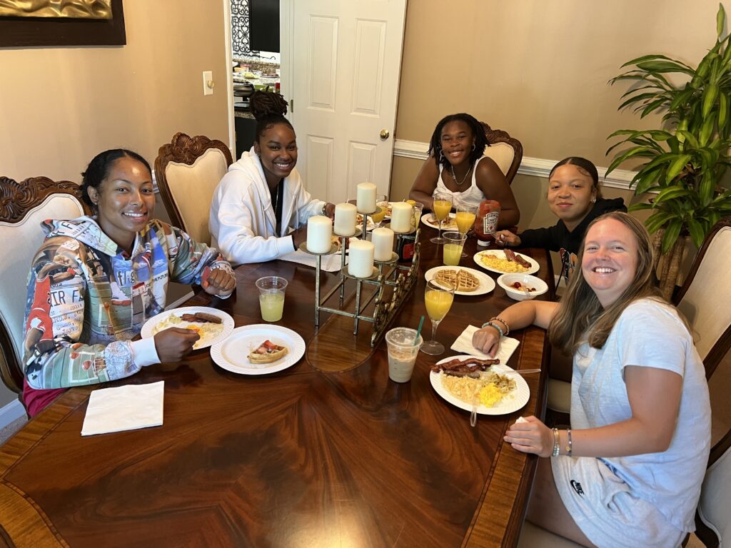 Five girls sit around a table eating breakfast