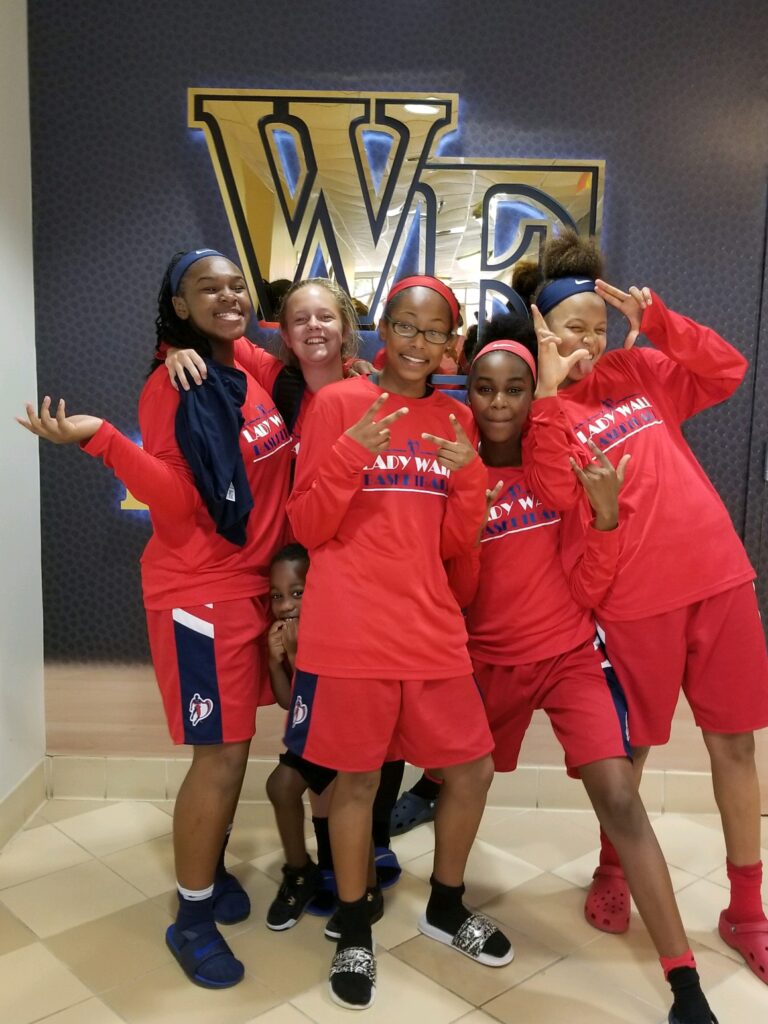 Five girls in basketball uniforms pose in front of Wake Forest logo
