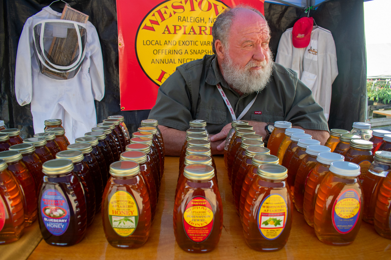 a man sitting at a table filled with bottles of honey.