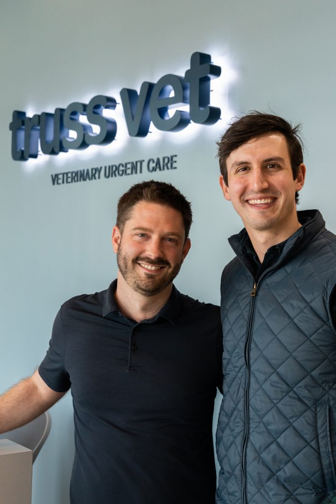 Brad Waffa (left) and CJ Casselli, co-founders of Truss Vet, stand beside a backlit dark blue sign of the company name in the lobby. "'Truss Vet' comes from this idea of bridging a gap in care, but also a truss is a triangle, which is where we get our start," Waffa said. "Truss," which sounds like "trust," alludes to the fact that they want clients to be able to trust the personnel as well.