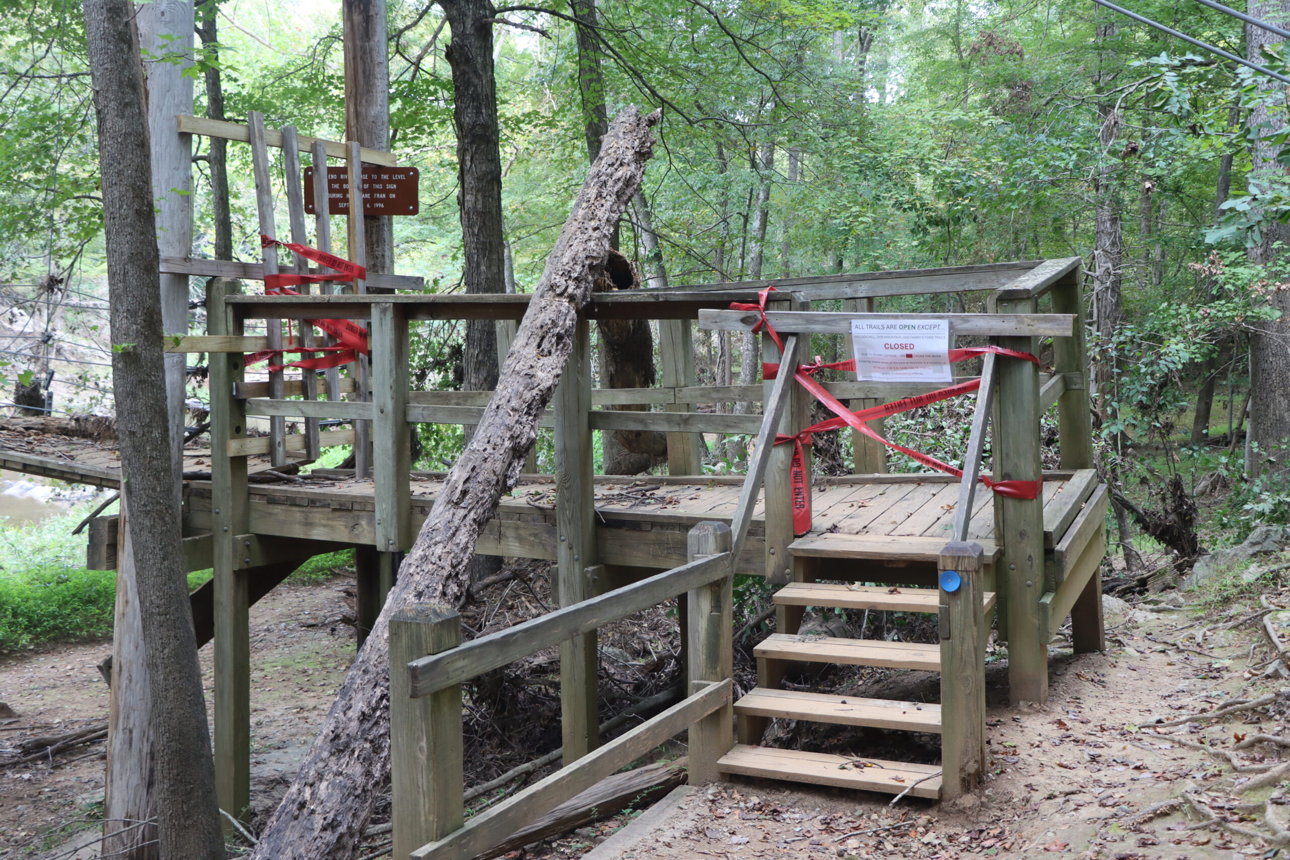A wooden bridge with red tape and a fallen tree on top of it.