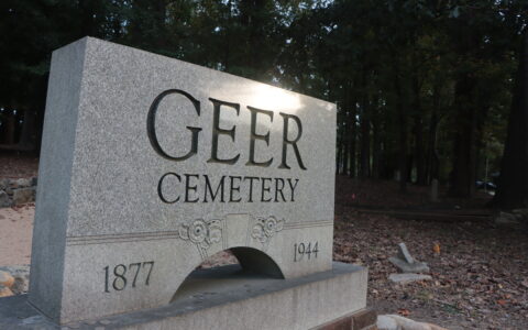 A gray stone plaque near the entrance of Geer Cemetery in Durham, North Carolina. On either side of the plague are dates, 1877 and 1944.
