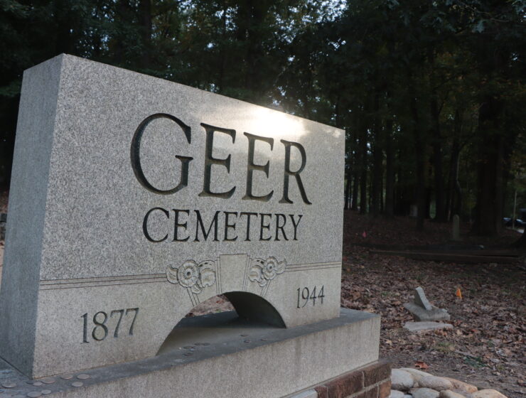 A gray stone plaque near the entrance of Geer Cemetery in Durham, North Carolina. On either side of the plague are dates, 1877 and 1944.