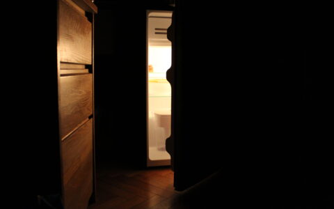 An open fridge in a dark dorm room.