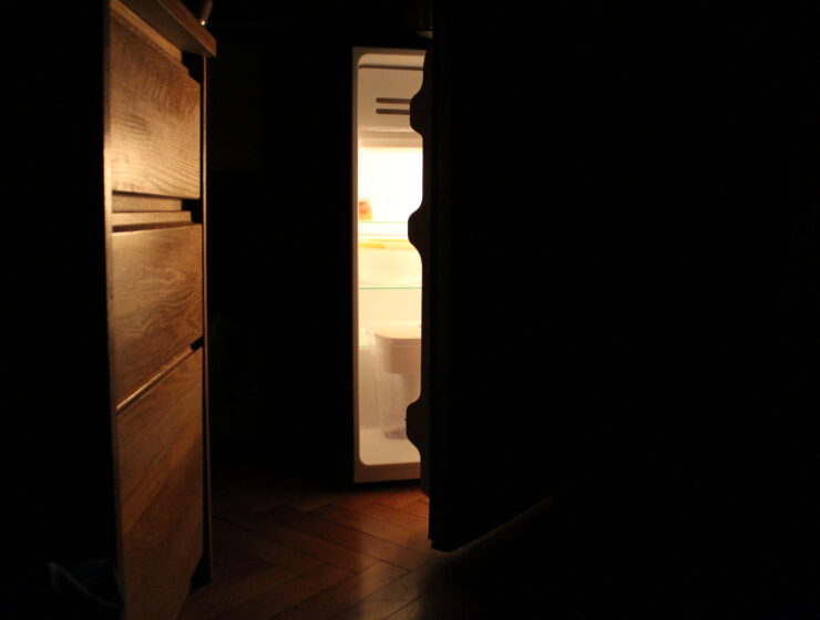 An open fridge in a dark dorm room.