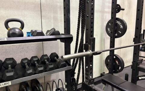 dumbbells, kettle bells, and weight plates on a stand. A squat rack and empty bench.