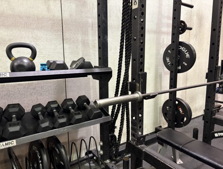 dumbbells, kettle bells, and weight plates on a stand. A squat rack and empty bench.